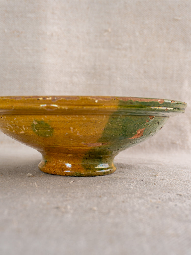 Antique French Provençal compotier with green and ochre glaze on textured beige fabric, shallow round ceramic form.