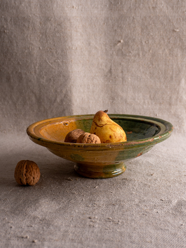 Antique French Provençal compotier with green and ochre glaze, displayed with pears and walnuts on beige textured fabric.