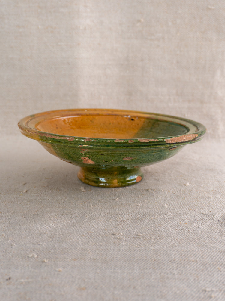 Antique French Provençal compotier, late 19th century, green and ochre glaze, small pedestal base, on beige textured fabric.