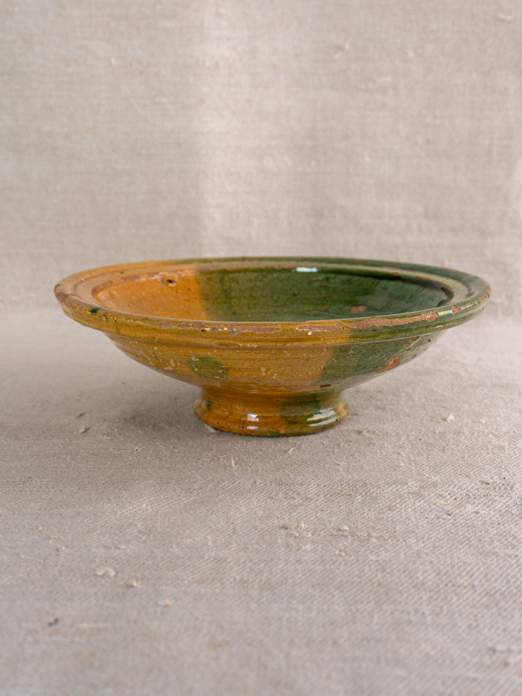 Antique French Provençal compotier with green and ochre glaze, pedestal base, on textured beige fabric.