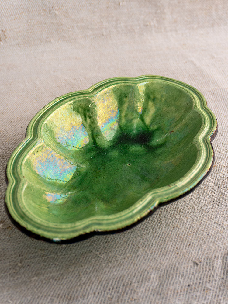 Lobed oval green-glazed earthenware dish inspired by antique French coupelle, on textured beige fabric background.