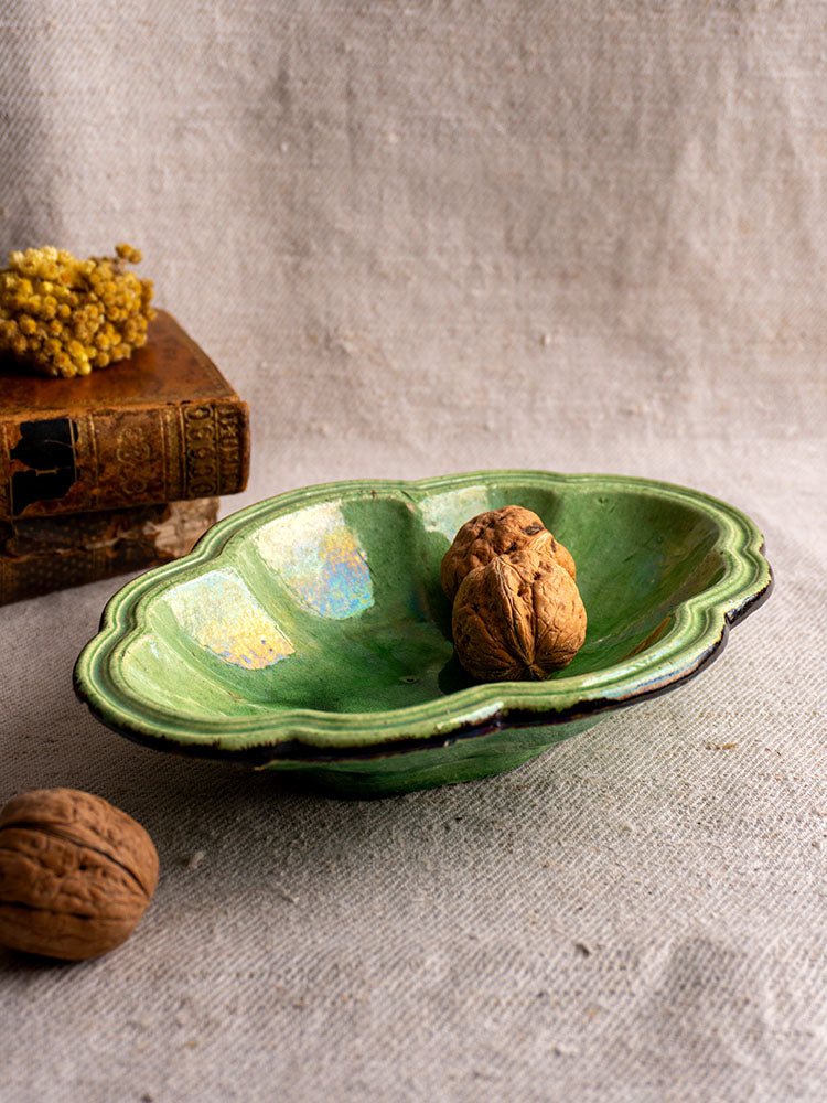 Antique French green glazed lobed oval coupelle with dark rim, likely Dieulefit, on textured beige fabric.