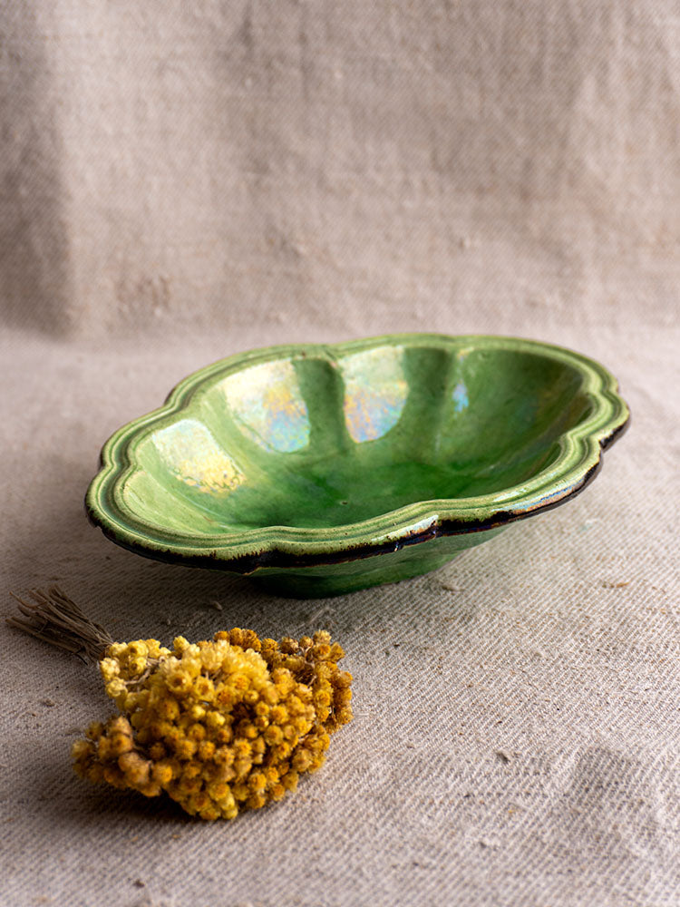 Antique French green glazed lobed oval dish on textured beige fabric with dried yellow flowers nearby.