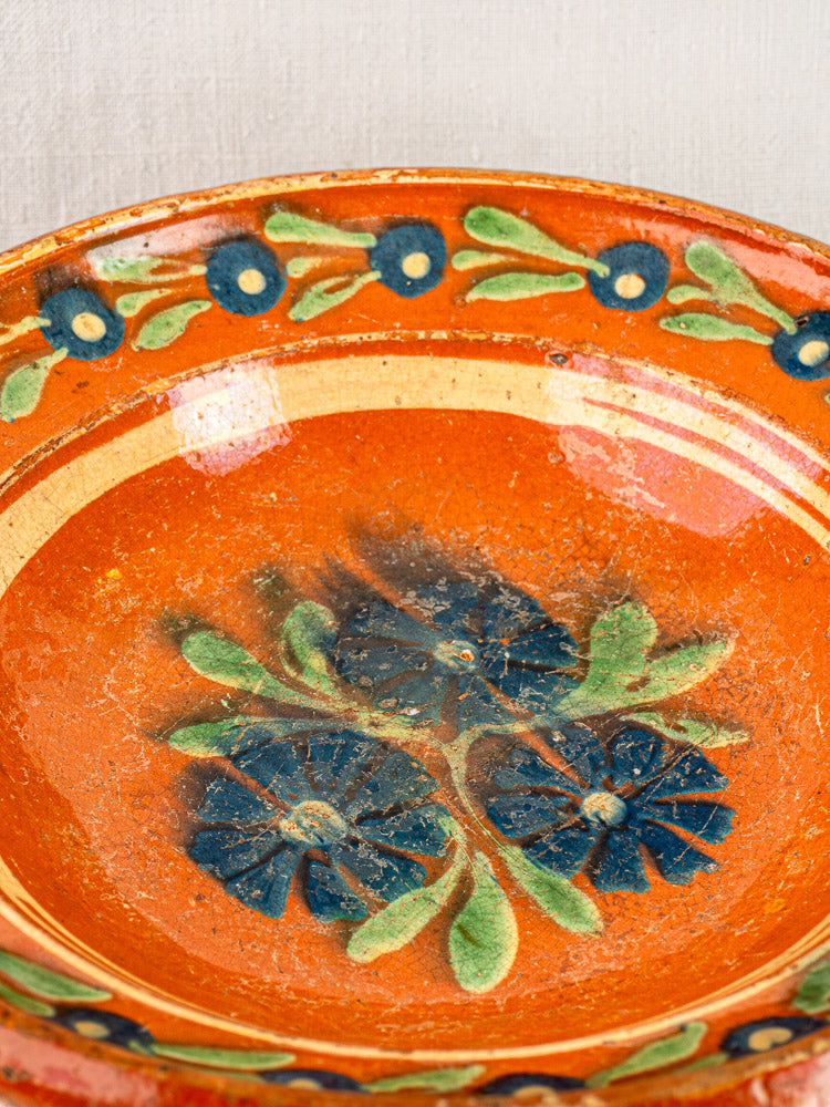 Antique French Alsatian Soufflenheim slipware plate with orange glaze and blue-green floral motifs, rustic timeworn finish.
