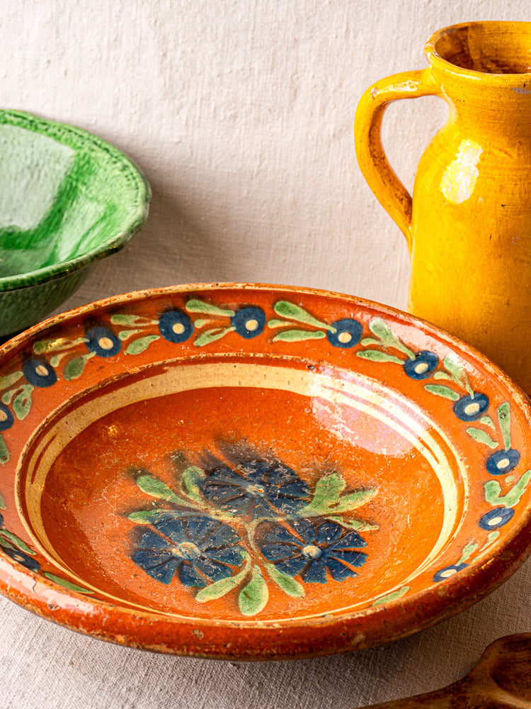 Antique French Alsatian Soufflenheim slipware plate with blue-green floral motifs and a decorative border on light fabric.