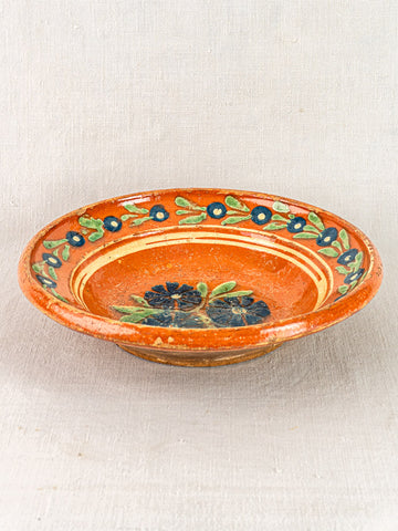 Antique French Alsatian Soufflenheim slipware plate with glossy finish, blue floral hand-painting, on neutral fabric background.