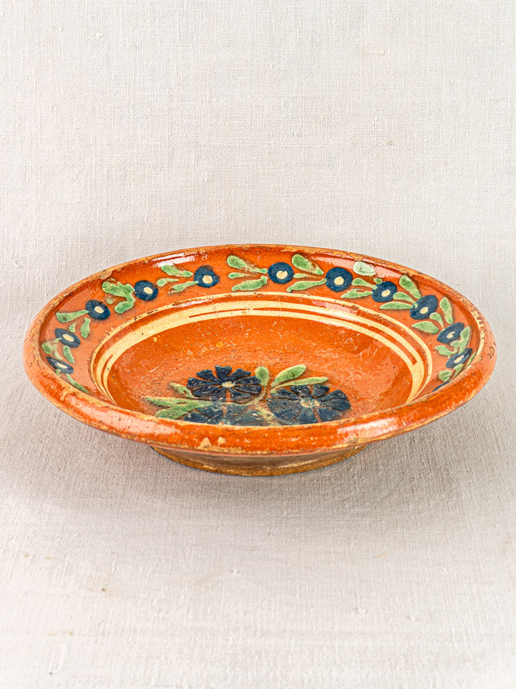 Antique French Alsatian Soufflenheim slipware plate with glossy finish, blue floral hand-painting, on neutral fabric background.