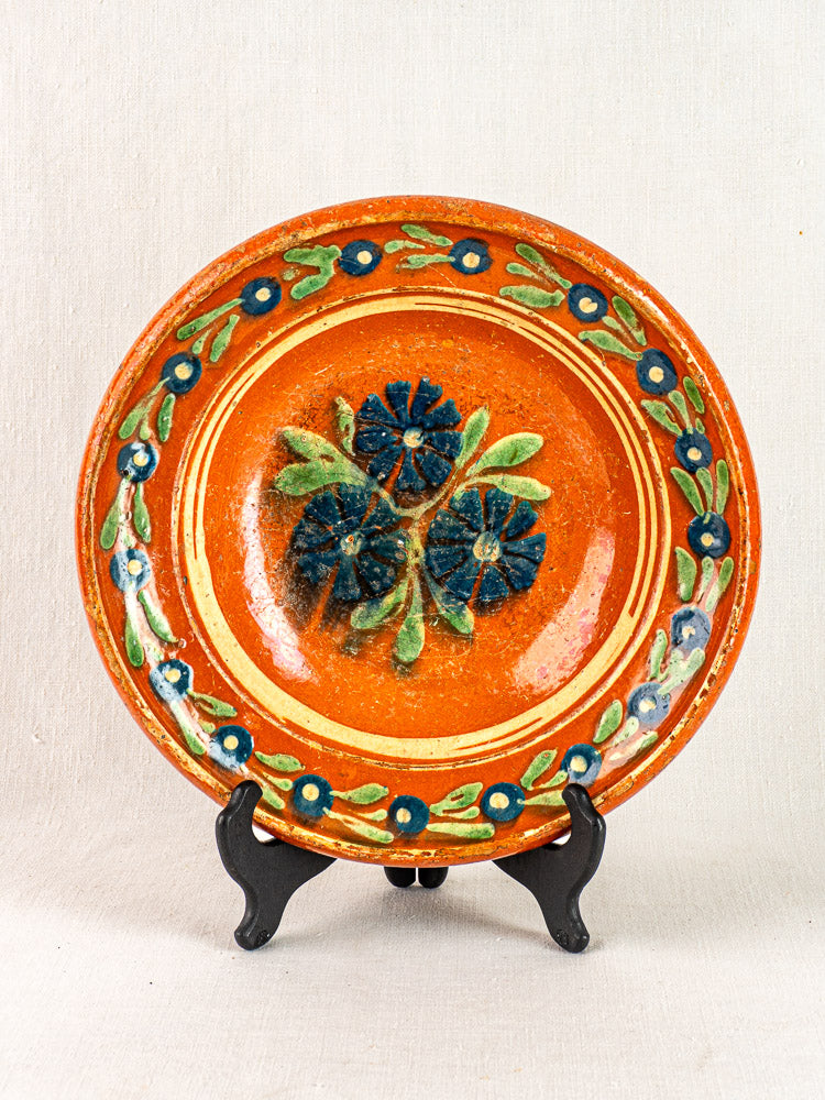 Antique French Alsatian Soufflenheim slipware plate with round orange body and blue floral motifs on black stand.
