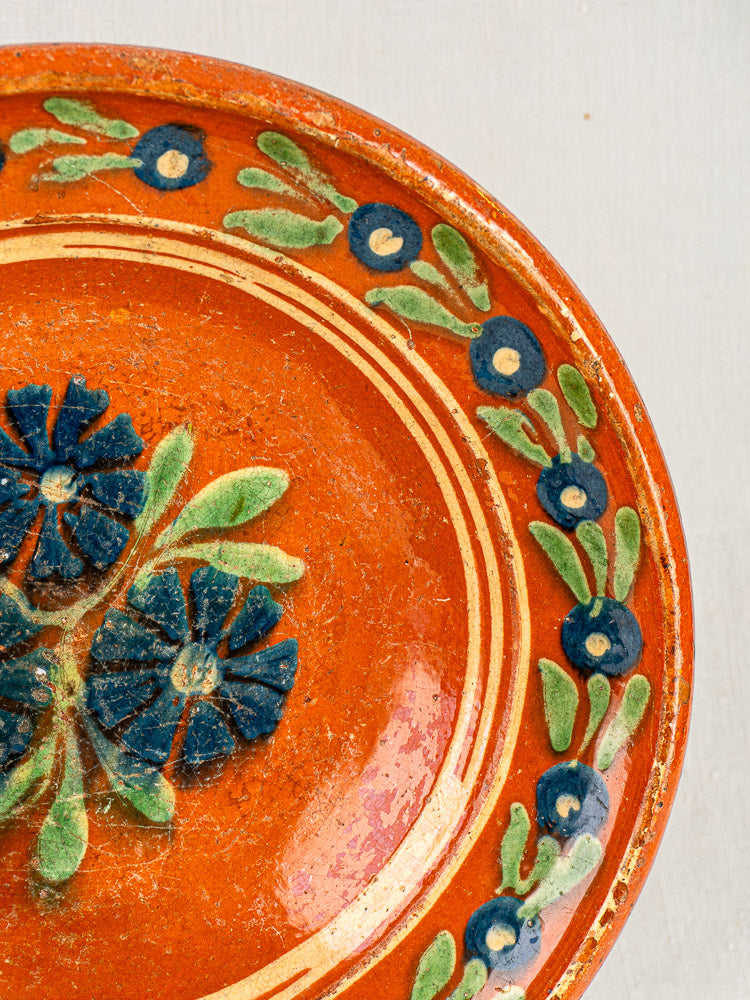 Antique French Alsatian Soufflenheim ceramic plate with hand-painted blue flowers, green leaves, and ornate borders on orange.