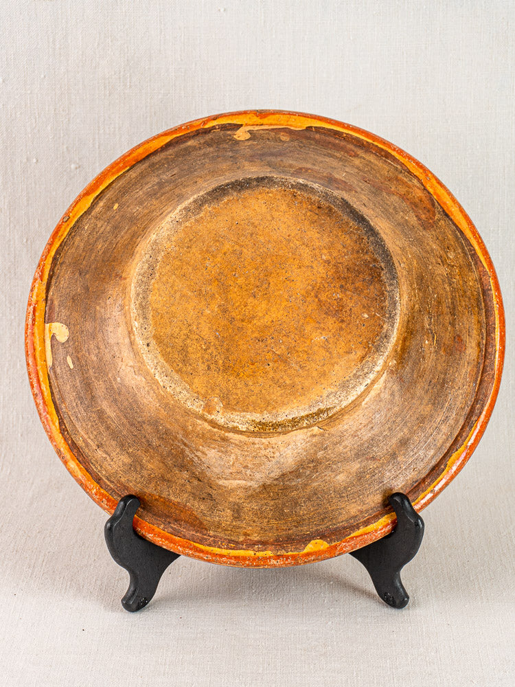 Antique French Alsatian Soufflenheim slipware plate with worn edges on black display stand, textured background.