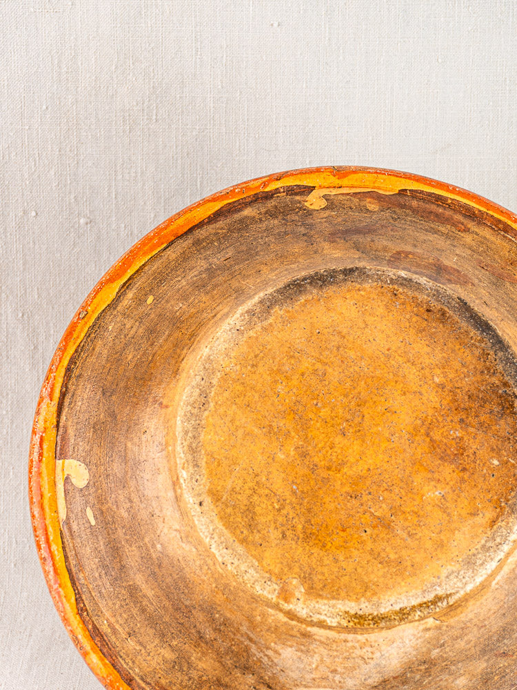 Antique French Alsatian Soufflenheim slipware plate, round with weathered surface and chips, on a light textured background.