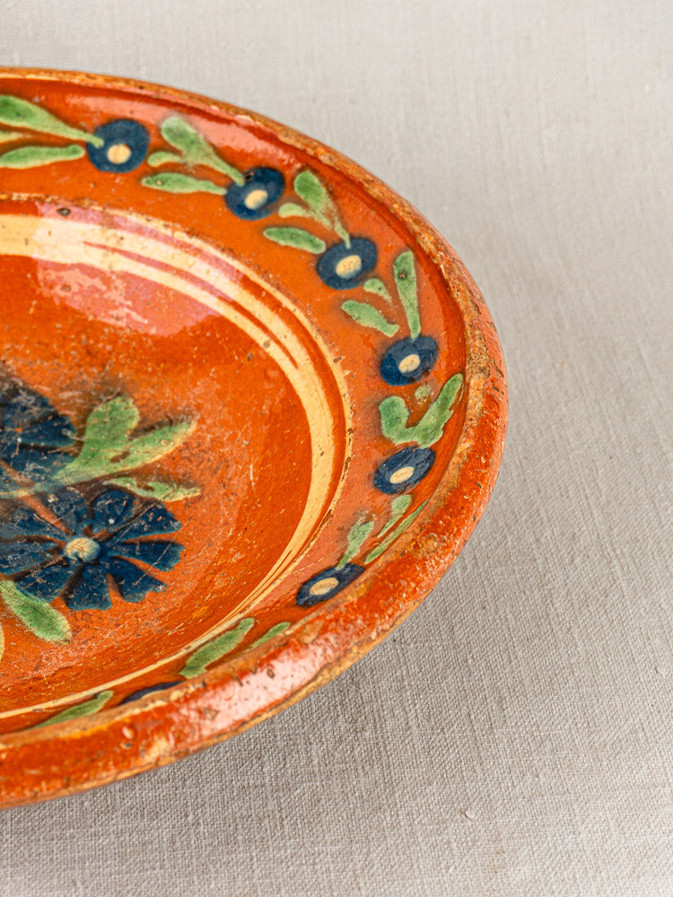 Antique French Alsatian Soufflenheim slipware plate with blue and green floral rim, on beige fabric background.