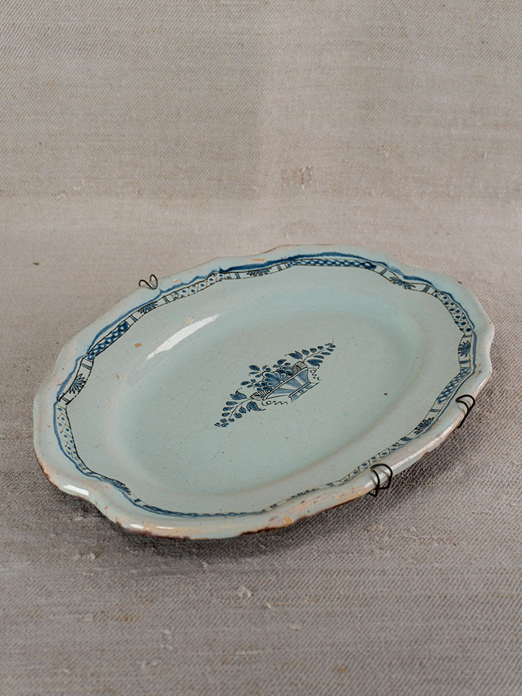 Antique French faience platter with scalloped edges, blue floral motif, staple repairs, on textured beige surface.