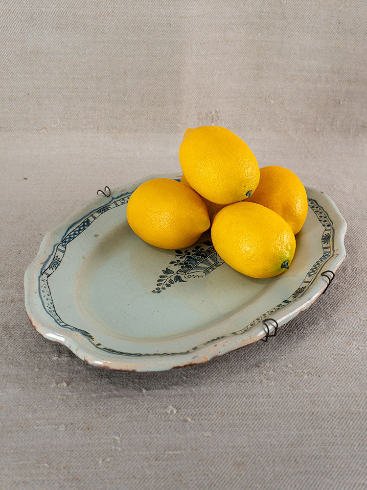 Antique French faience platter, Rouen Cul Noir, 19th century, blue patterns, with lemons on neutral fabric background.