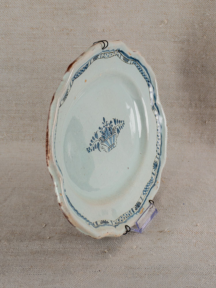 Antique French faience platter with scalloped edge and blue floral crown design, displayed on neutral fabric.