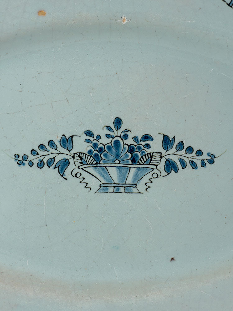 19th-century French faience platter with blue basket, leaves, and flowers on a pale, lightly crackled finish.