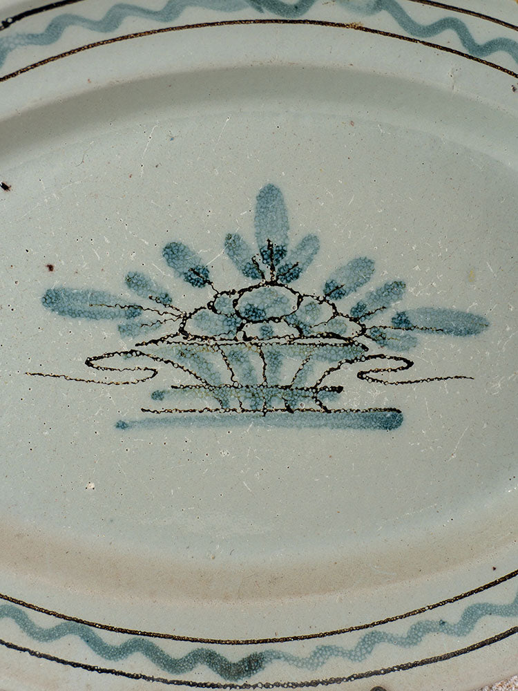 Antique French faience platter with blue floral and basket motif, stylized leaves, dots, and wavy Rouen border.