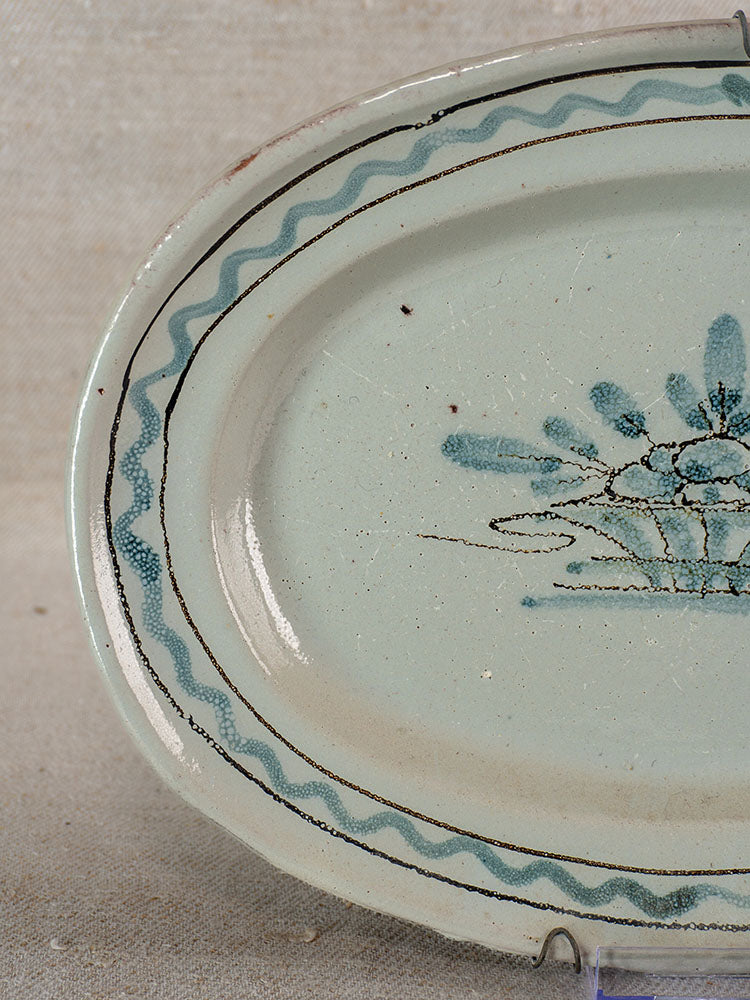 Antique French faience platter with crackled glaze, blue wavy border, and floral motif on neutral fabric background.