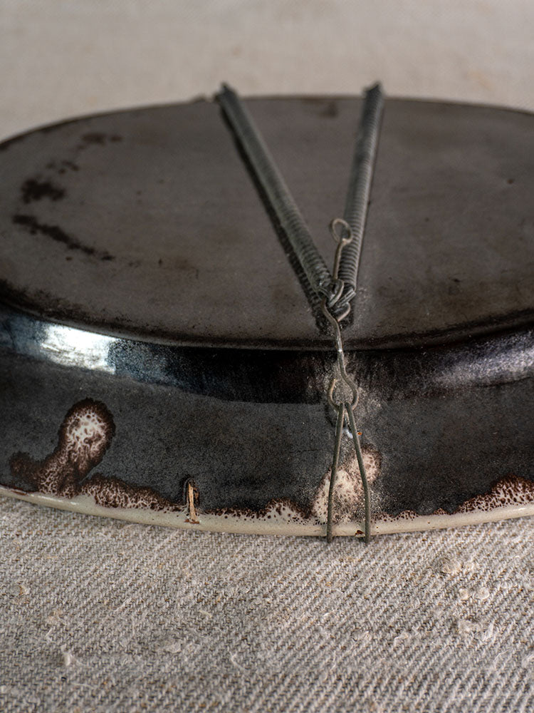 Back of antique French faience platter with wire hanger, slight edge discoloration, on textured fabric.