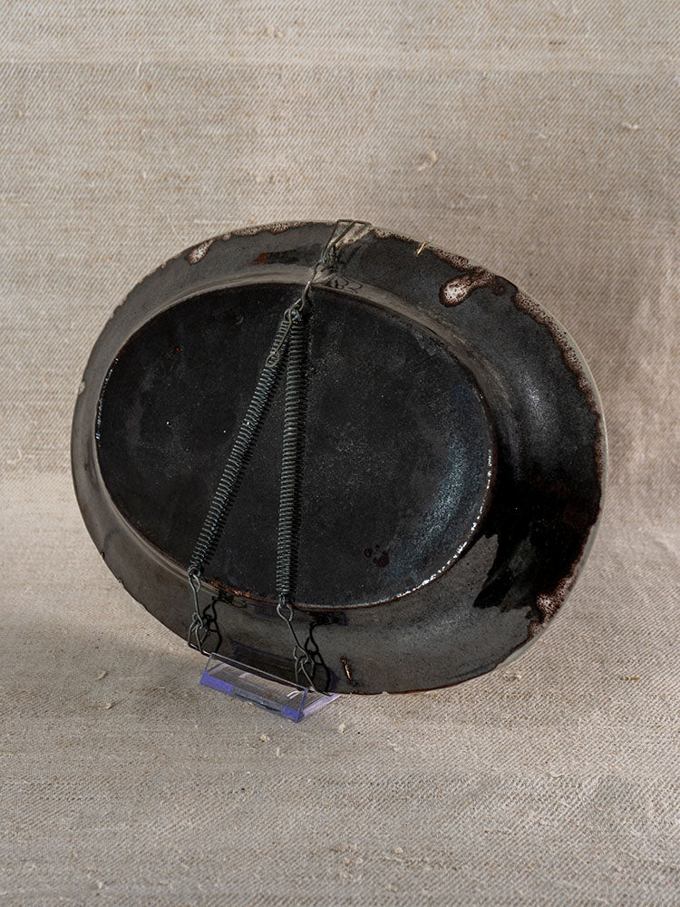 Antique French faience Cul Noir platter, oval with Rouen floral pattern, upright on wire supports against beige fabric.