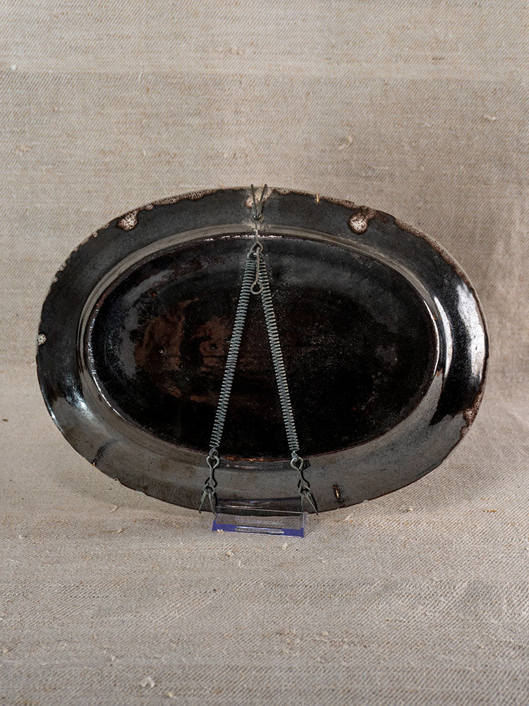 Antique French faience Cul Noir platter, oval and dark brown, glossy back, some edge wear; shown on metal stand.