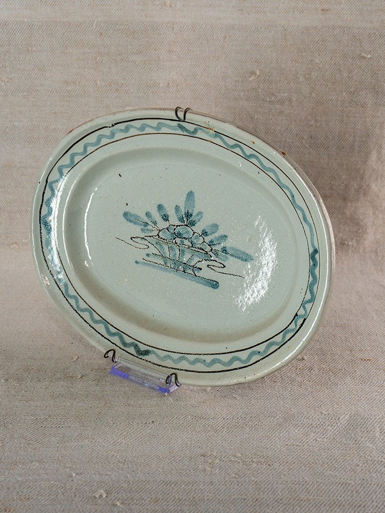 Antique French faience platter, oval with blue floral center and wavy rim, Decor Rouen style, on display stand.