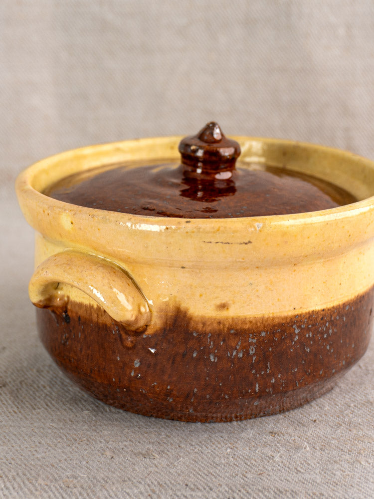 Early 20th-century French Marmite, yellow ochre and brown glazed earthenware with lid, on neutral textured fabric.