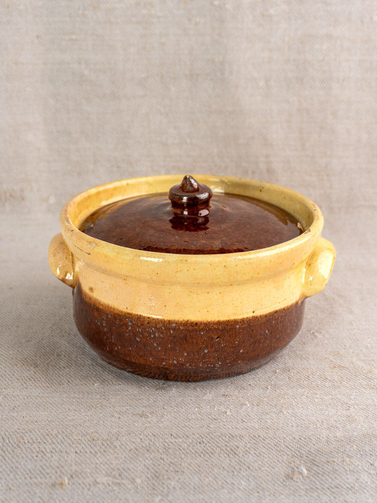 Antique French marmite, early 20th-century earthenware pot with lid, brown and ochre glaze on beige textured surface.