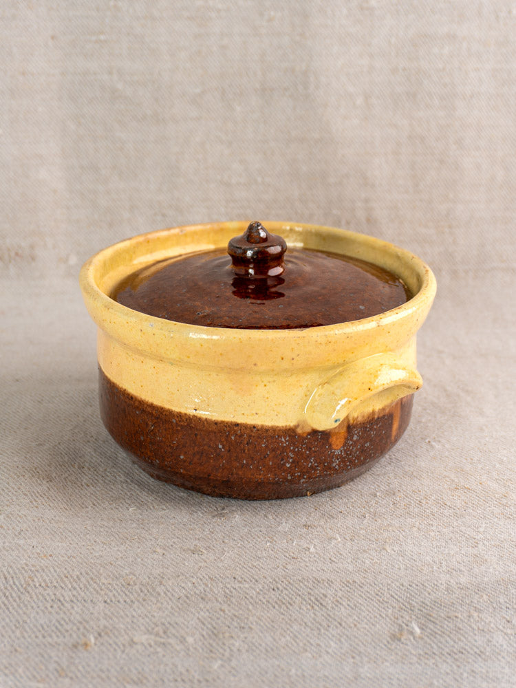 Antique French marmite in yellow ochre and brown glazed earthenware on textured beige fabric background.