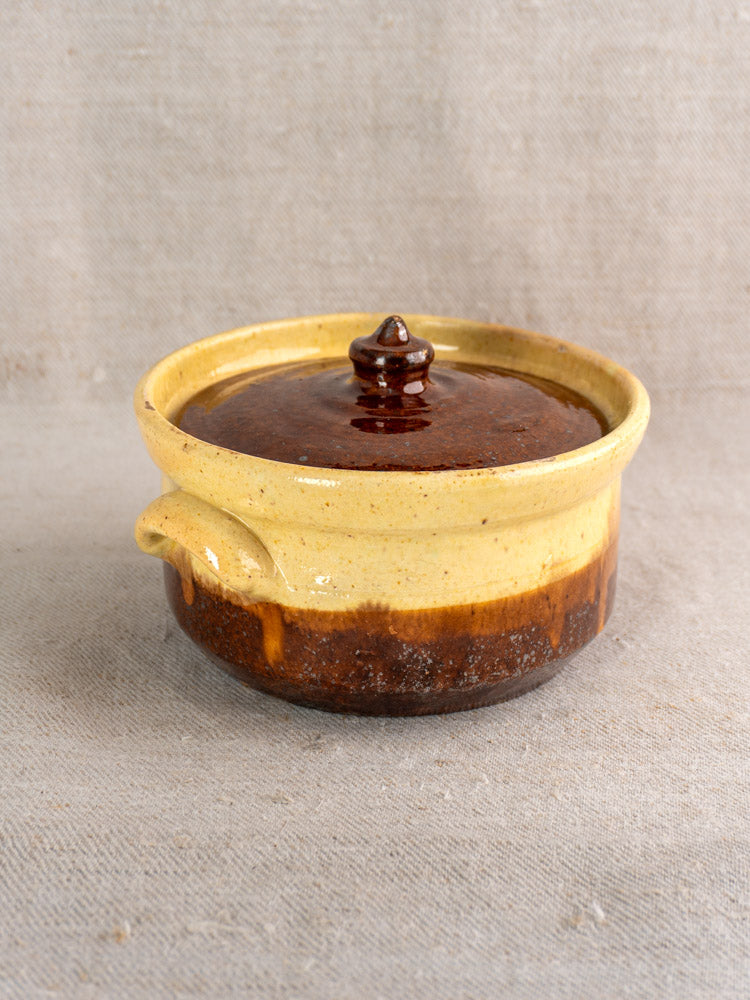 Early 20th century French yellow ochre and brown glazed earthenware marmite casserole with knobbed lid on neutral surface.