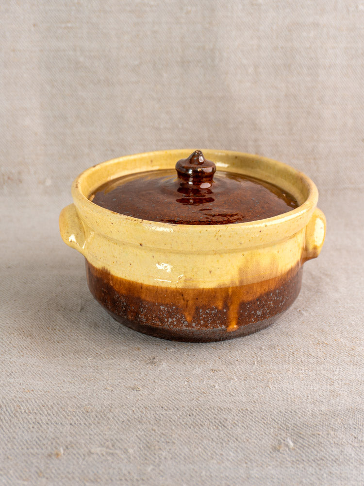 Antique French marmite, early 20th-century yellow ochre and brown glazed earthenware, on neutral fabric background.