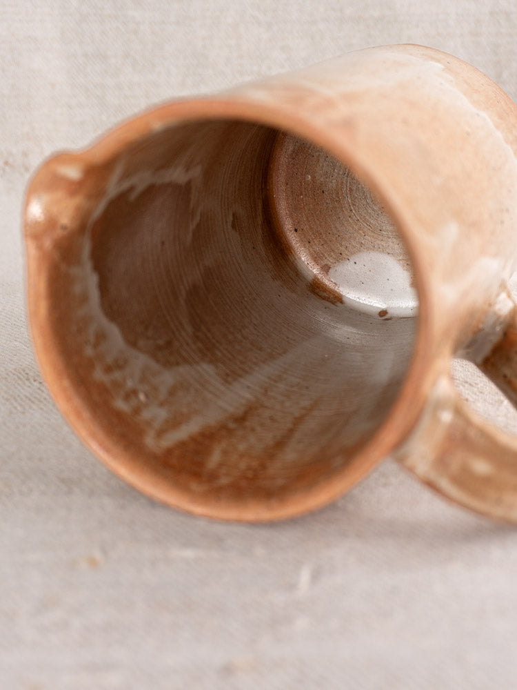 Antique French stoneware salt glaze cruche, mid-20th century, on its side showing glazed interior atop neutral fabric.