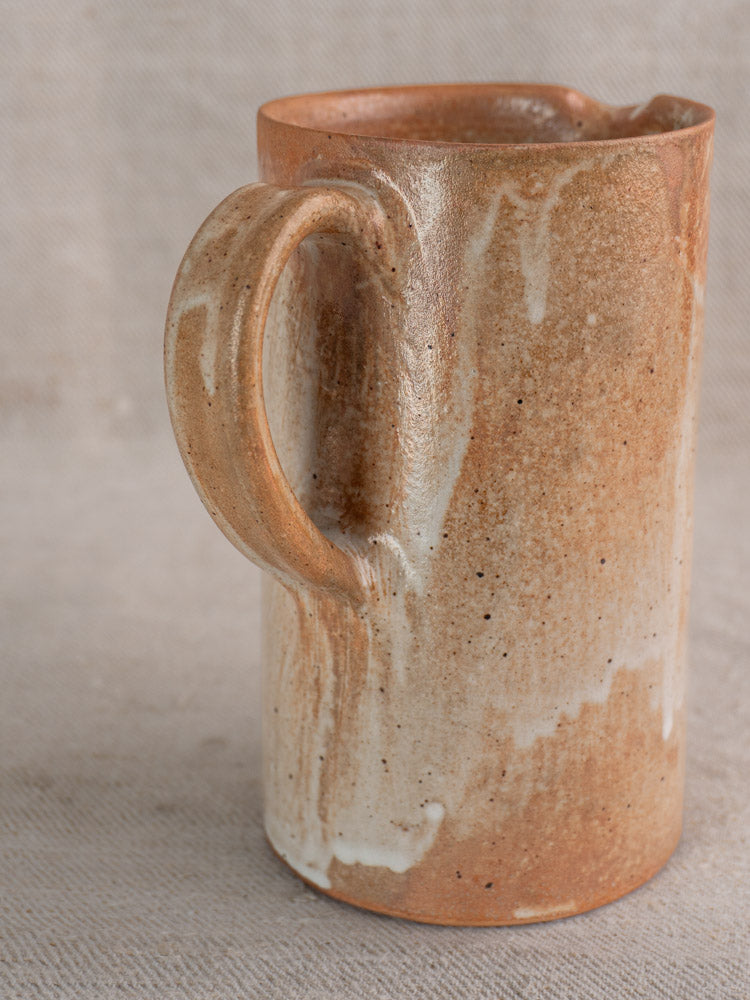 Antique French stoneware cruche with salt glaze in rustic brown and cream on a textured beige surface.