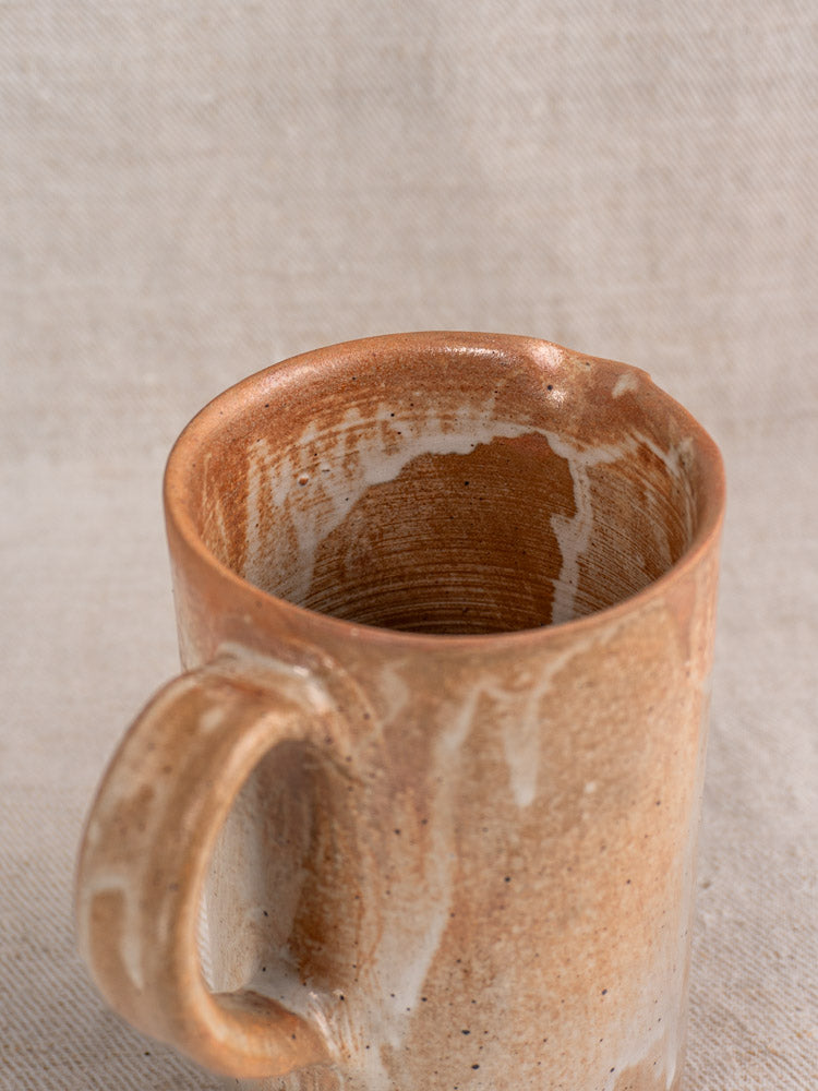 Antique French stoneware cruche with brown and white salt glaze, handle and interior visible on textured fabric.