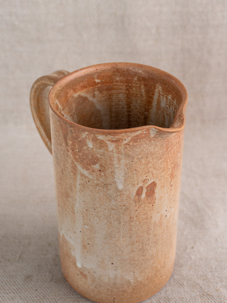 Mid-20th century French stoneware cruche with handle, spout, and salt glaze drips on beige textured fabric.