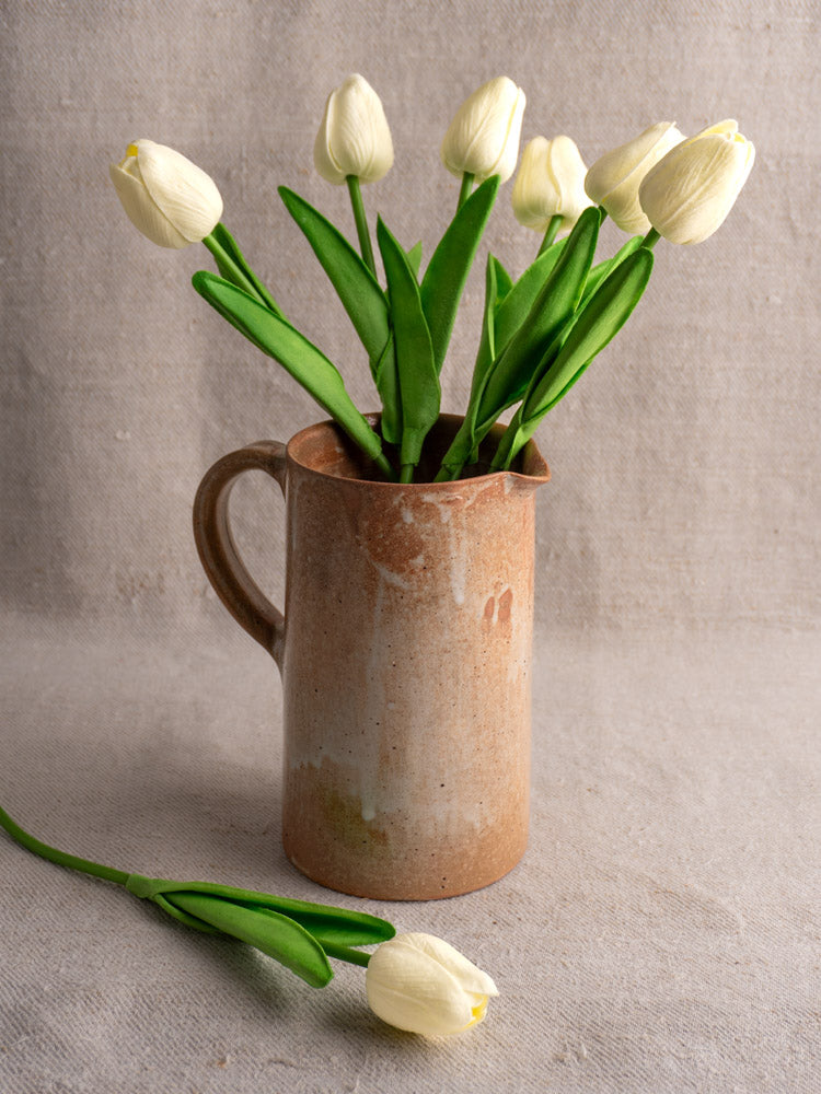 Mid-20th century French stoneware salt glaze cruche with white tulips, on gray fabric with neutral cloth backdrop.