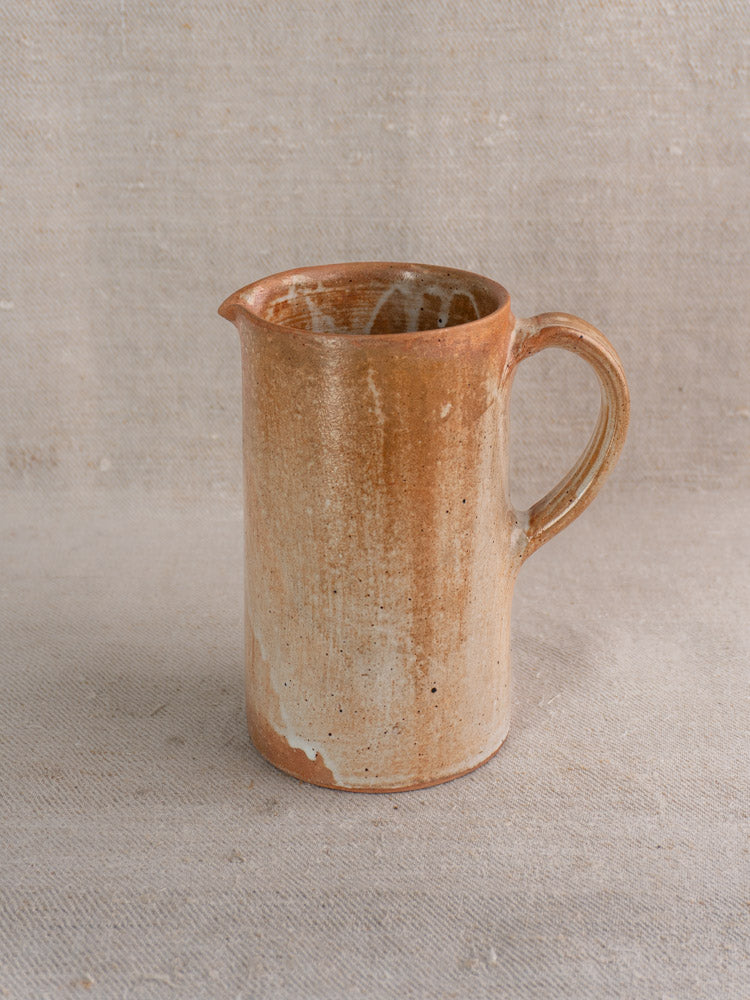 Antique French stoneware cruche with handle and rustic brown salt glaze on neutral textured fabric background.