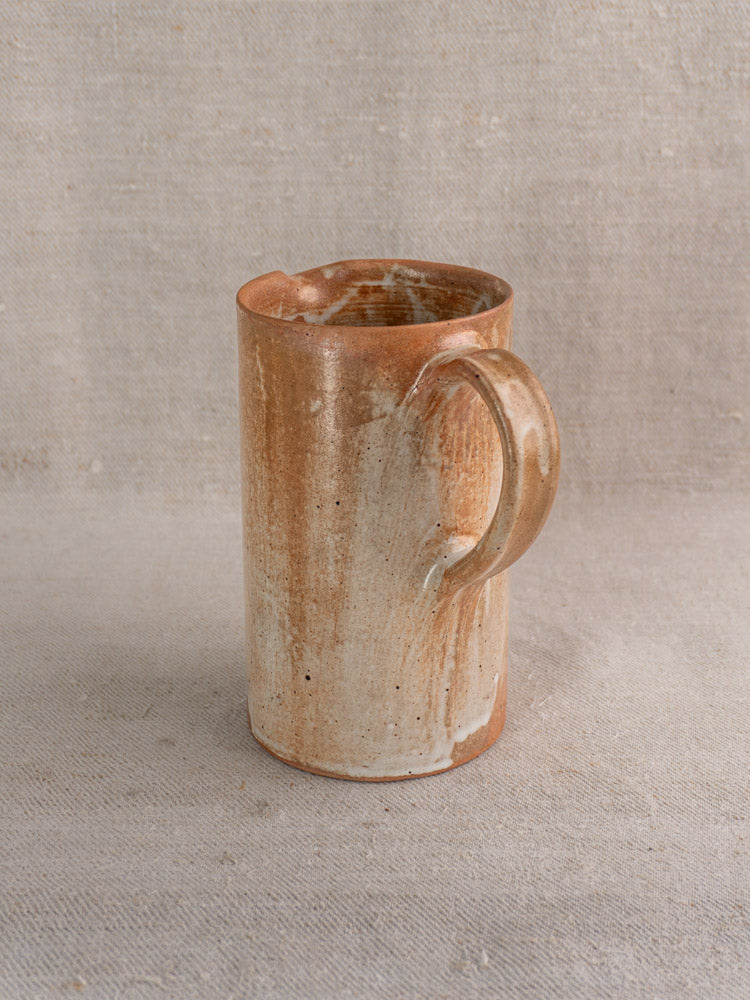 Antique French stoneware cruche with rustic brown and beige salt glaze, large handle, on textured fabric.