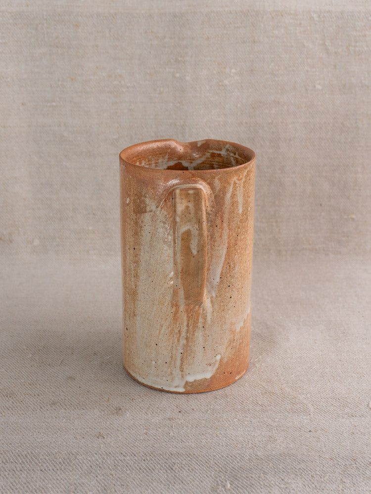 Mid-20th century French stoneware cruche with brown and beige salt glaze on textured light fabric background.