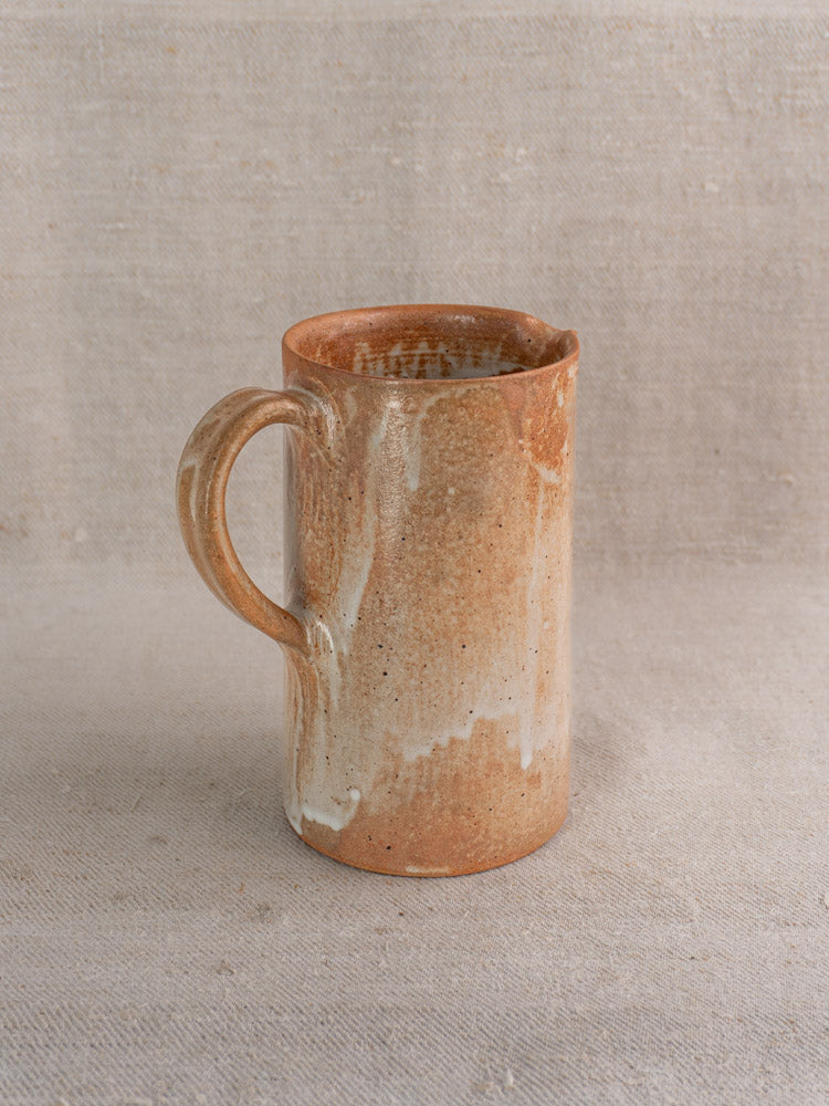 Antique French stoneware pitcher with salt glaze and rustic handle on light beige fabric.