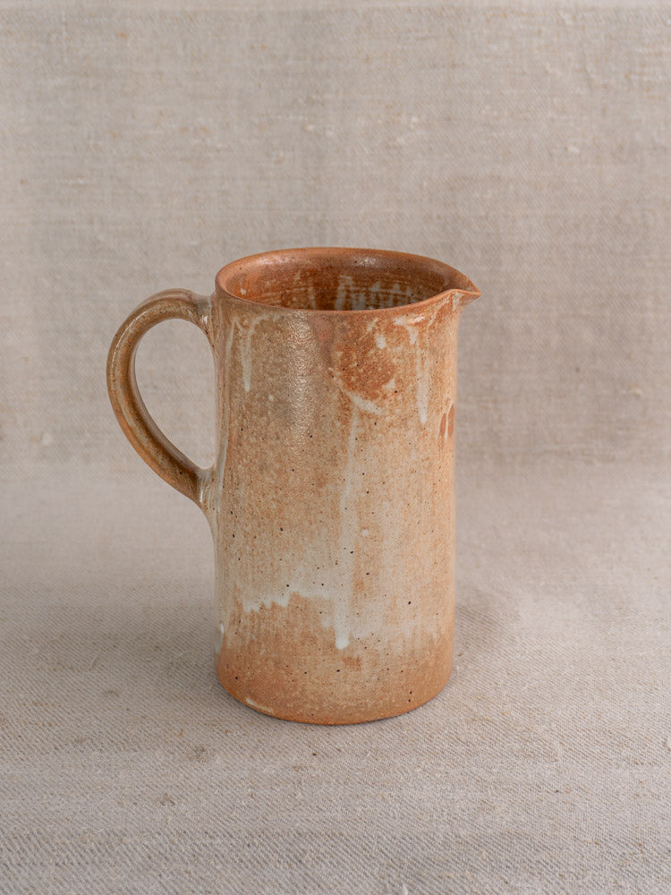Mid-20th century French stoneware cruche with handle, spout, and speckled glaze on neutral textured fabric.
