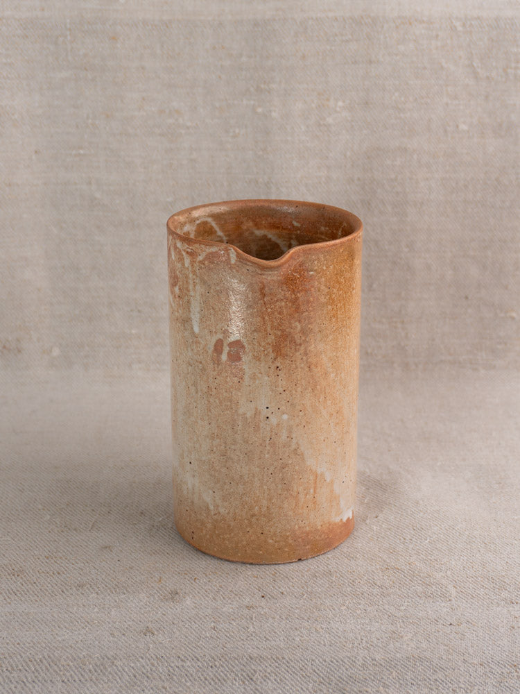 Antique French stoneware cruche with warm brown salt glaze on neutral textured fabric background.