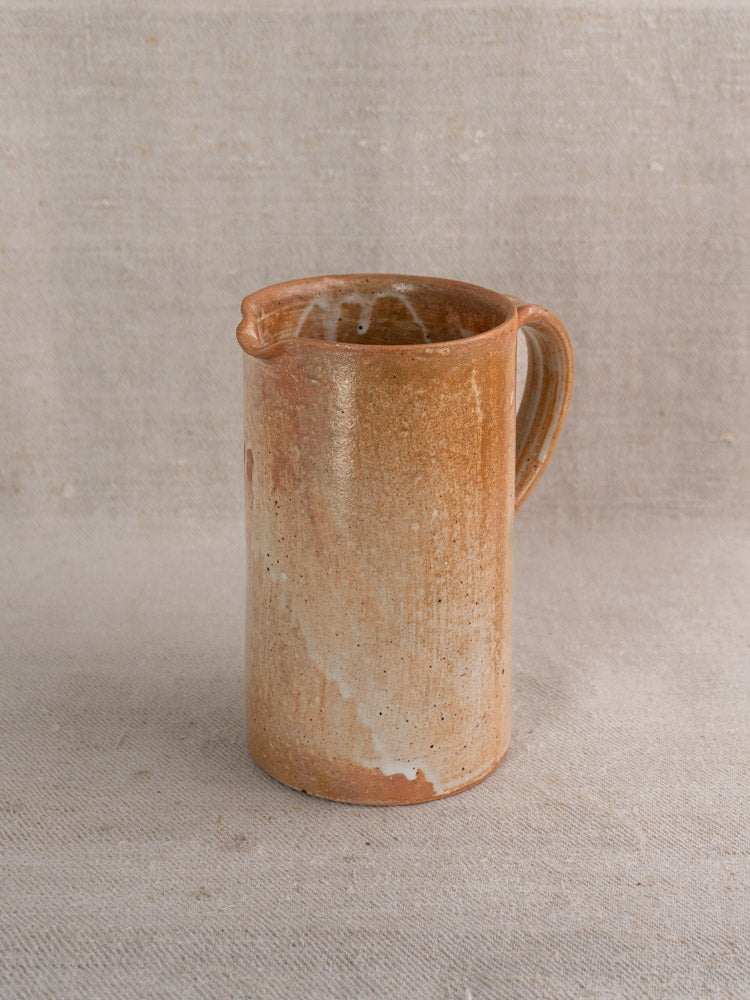 Antique French stoneware cruche with handle and spout on textured beige fabric, classic vintage pottery charm.