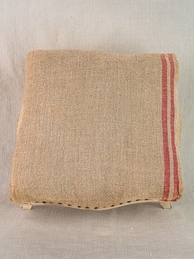 Antique French footstool with painted Louis XV frame, hemp upholstery, and burlap cushion with red stripes.