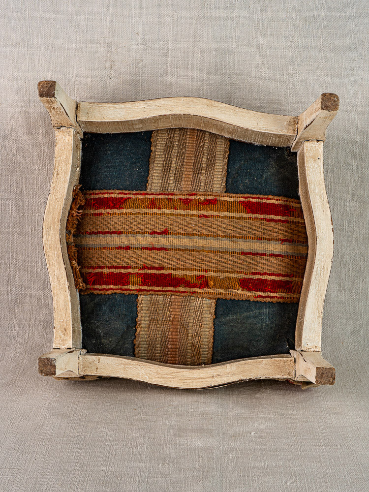 Upside-down wooden chair frame reveals woven blue and red striped upholstery reminiscent of French torchon.