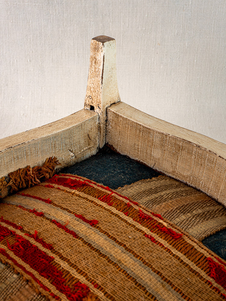 Antique French Louis XV footstool with worn painted frame and frayed striped hemp upholstery.
