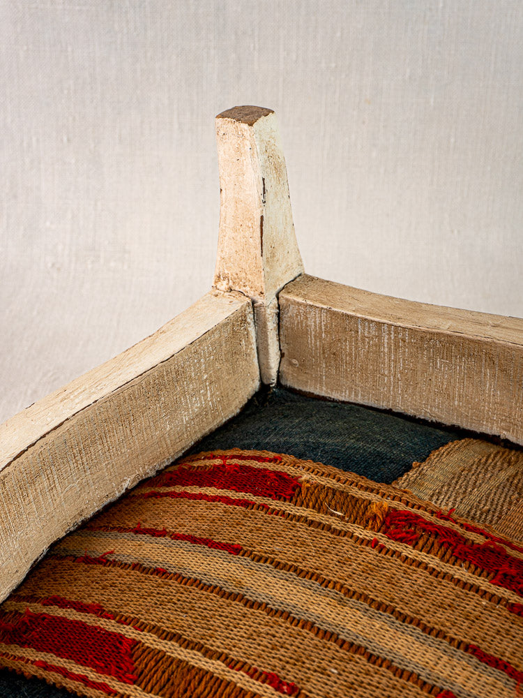 Antique French footstool with painted Louis XV frame and striped hemp torchon upholstery, neutral fabric background.