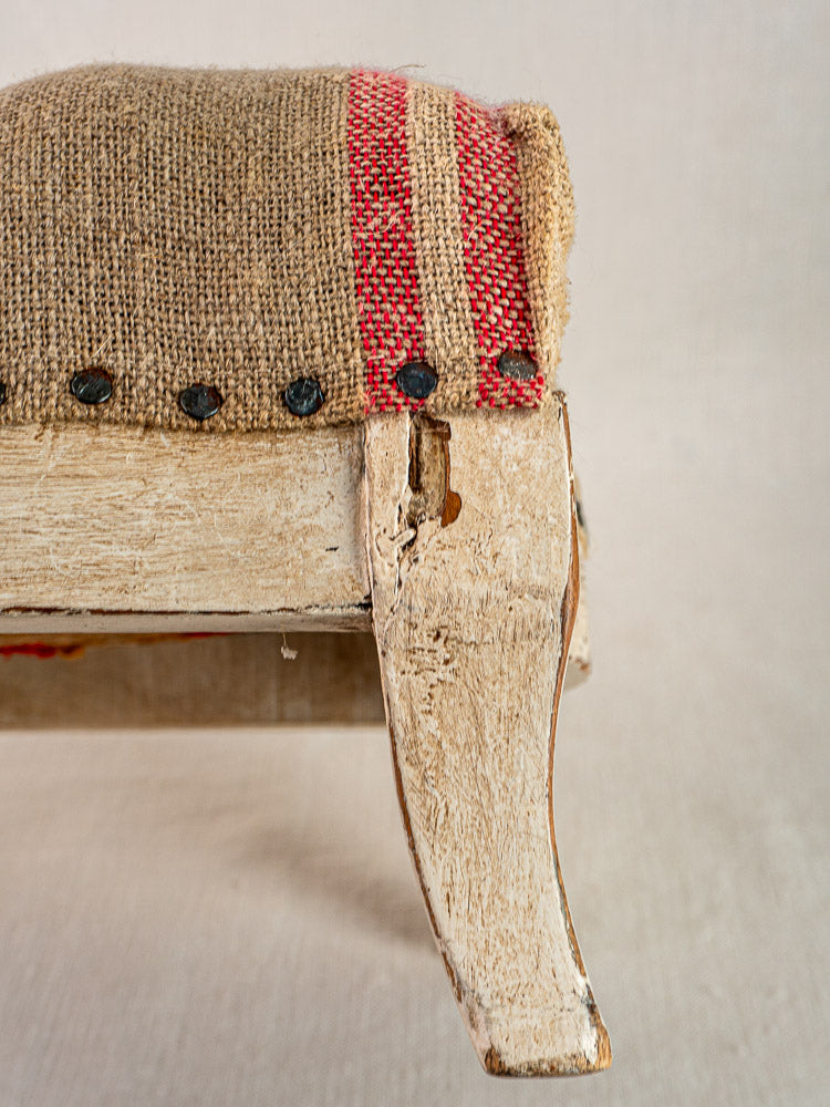 Antique French Louis XV footstool with distressed white frame, hemp torchon seat, and red stripes.