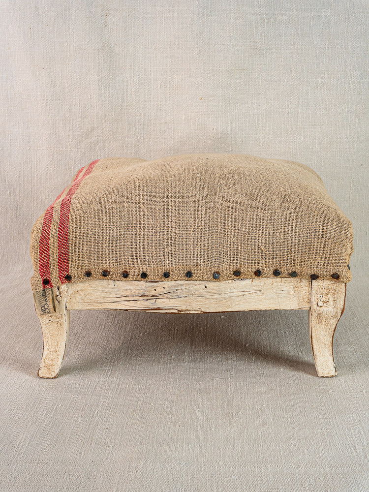 Antique French Louis XV footstool with painted frame, hemp burlap upholstery, red stripes, nailhead trim.