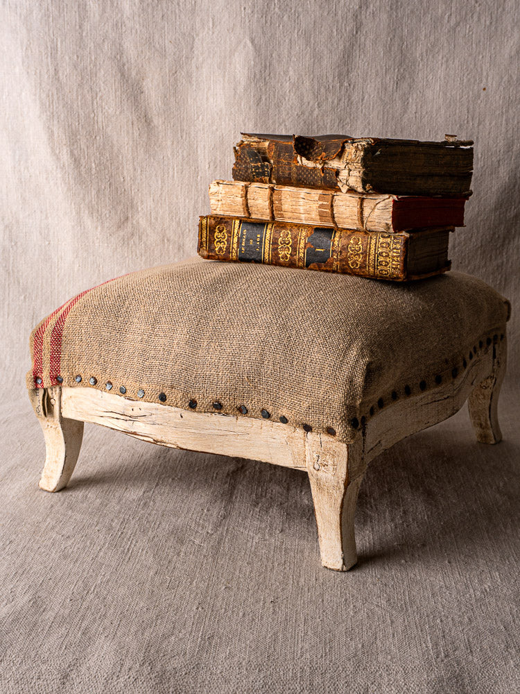 Antique French Louis XV footstool with painted frame, hemp burlap upholstery, red stripes, nailhead trim.